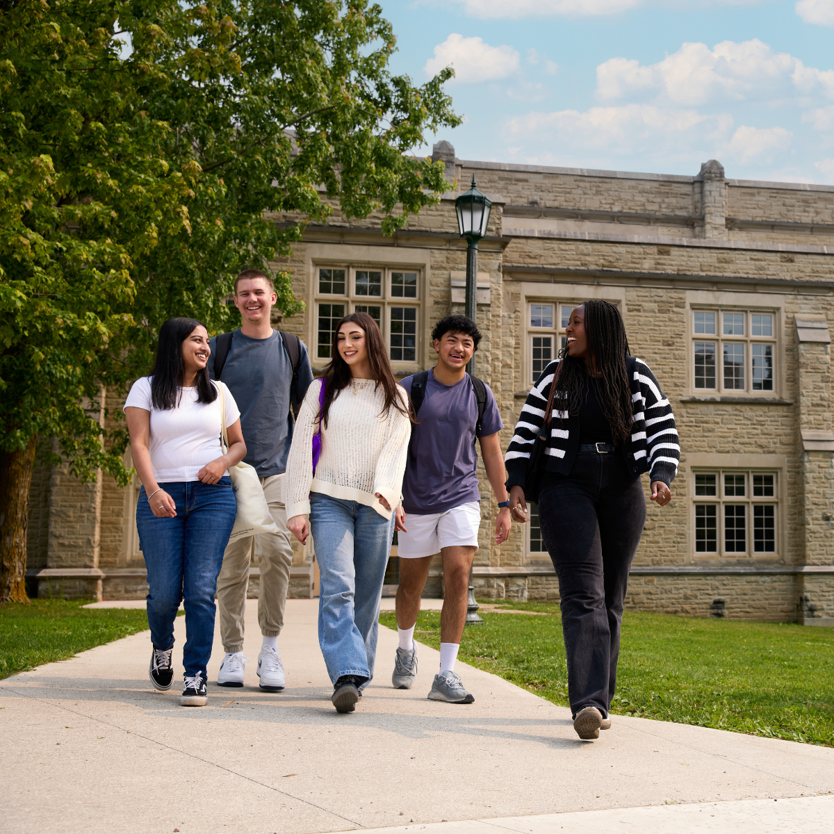 a group of students walking, smiling on campus on a sunny day.