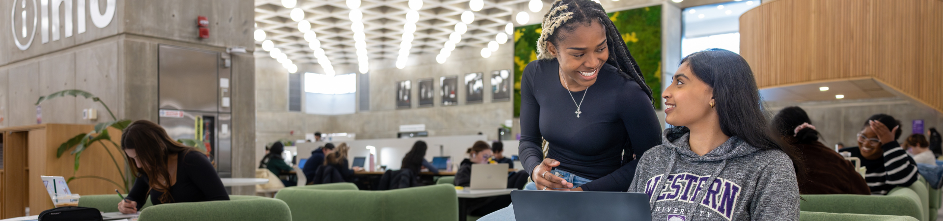 Two students huddle around a laptop in Weldon library.
