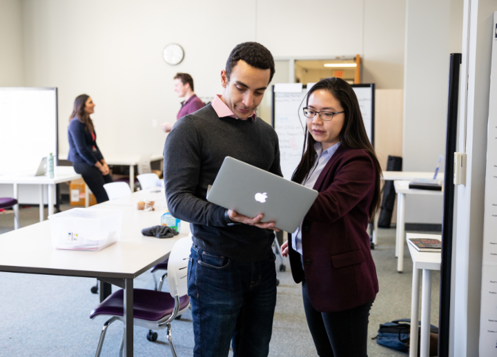 two people looking at a laptop together, while standing.