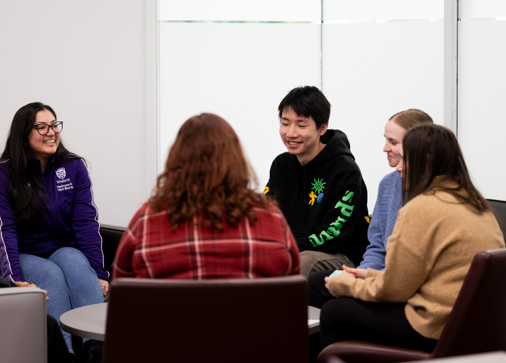 A group of students, smiling and sitting in a circle chatting.