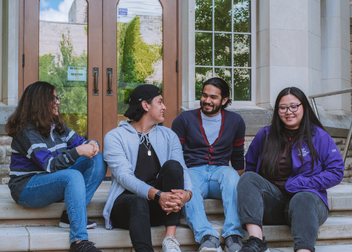 four students sitting on steps, smiling and chatting.