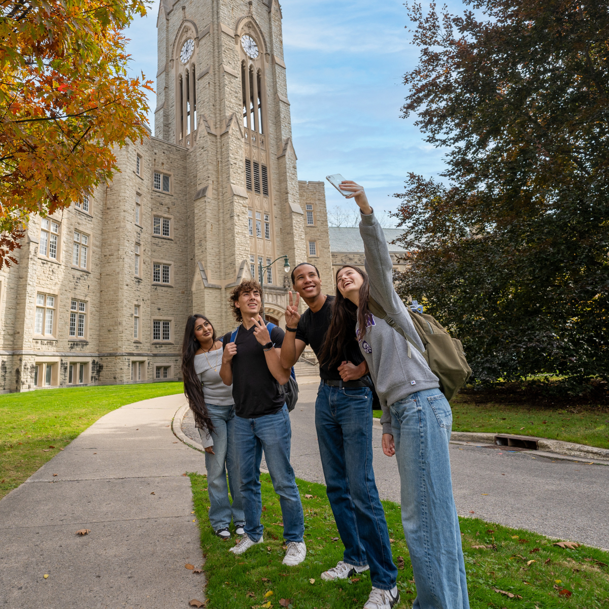 students taking a selfie photo in front of Middlesex College on a sunny day.