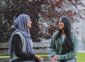 Two students sitting on a bench chatting