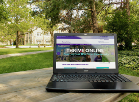 A laptop sitting on a picnic table on campus with the Thrive online website displayed