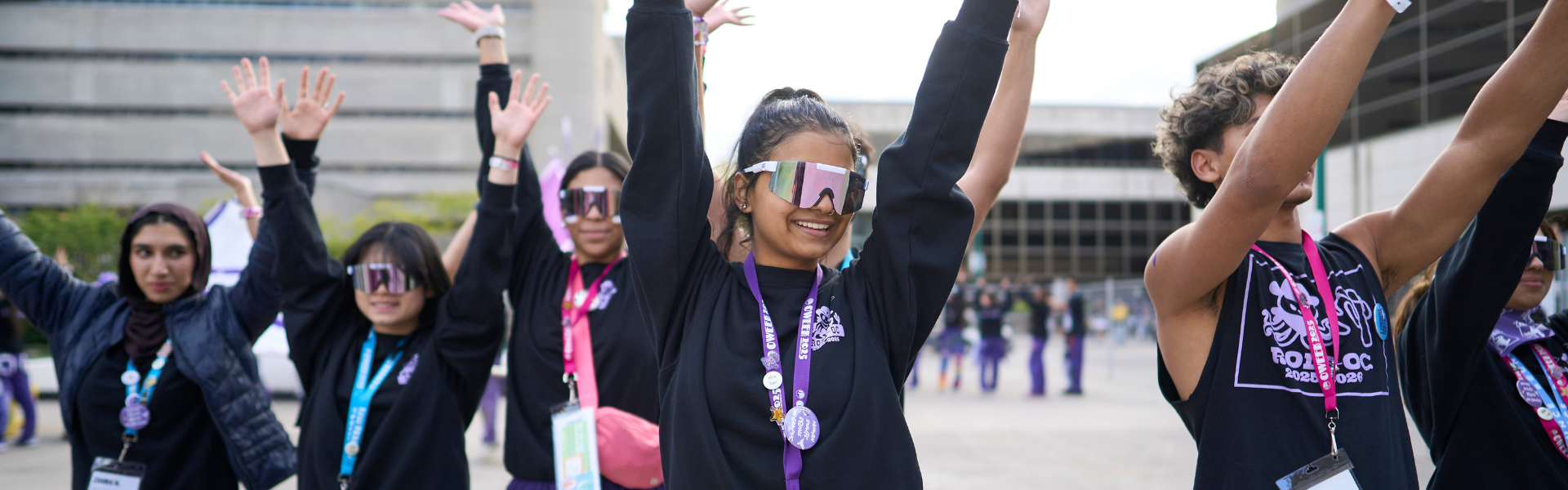 a group of students with their hands up, wearing purple.