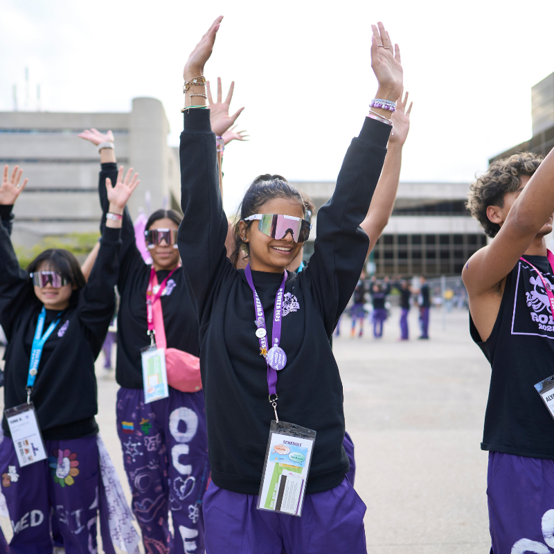 a group of students with their hands up, wearing purple.