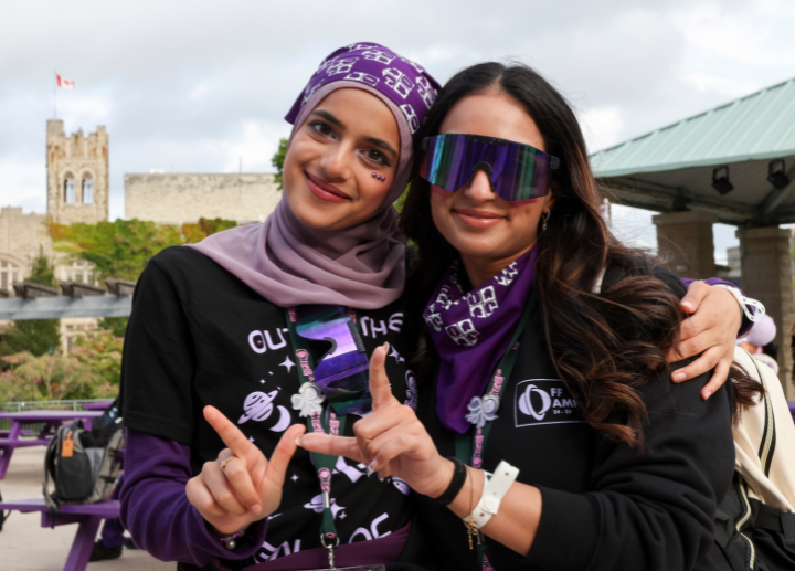 two students smiling for a photo, holding their hands in the shape of a W.