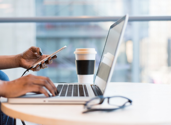 View of person's hands while working at a laptop with a cell phone.